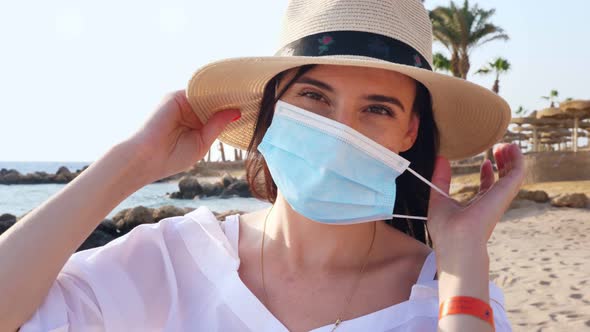 Portrait of Woman in Sun Hat, Who Takes Off Her Protective Mask, Against Sea Background, Beach 