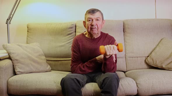 Elderly Man Doing Exercises with Dumbbells While Sitting on Couch at Home