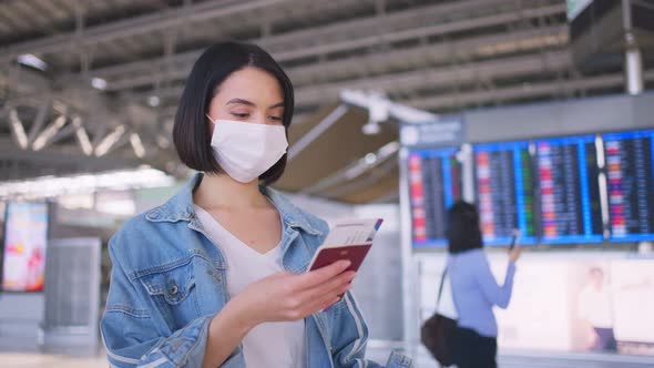 Asian woman passenger wearing face mask, walking in airport terminal to boarding gate to airplane.