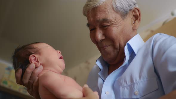 An Old Asian Grandfather Holds a Crying Newborn Baby in His Arms