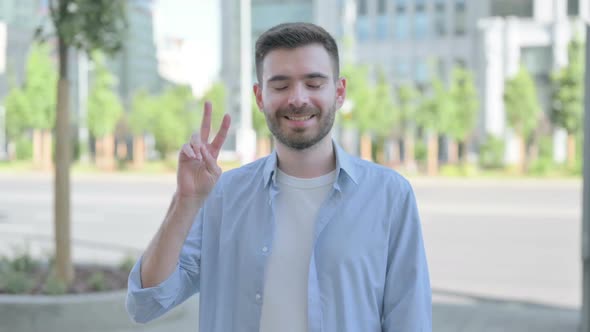 Outdoor Portrait of Young Man with Victory Sign