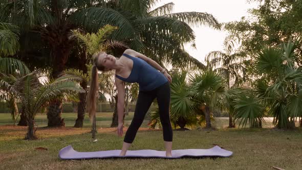 Young Woman Standing on Yoga Mat and Doing Warm Up Exercise at Outside