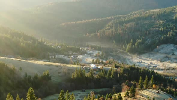 Zoom in Drone View of Houses Located Amidst Trees Near Hills on Sunny Day in Nature - Aerial View