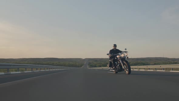 Biker Rides on Highway Against Background of Sky and Hills Presses Gas and Goes Around the Camera