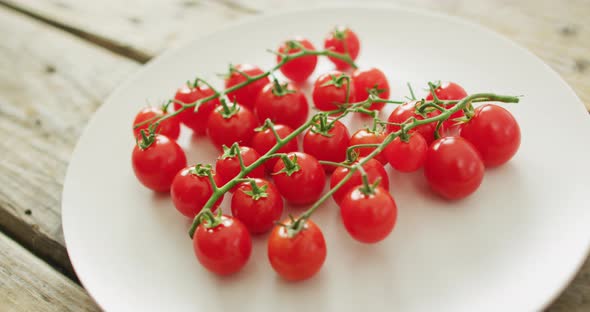 Video of fresh cherry tomatoes on white plate over wooden background