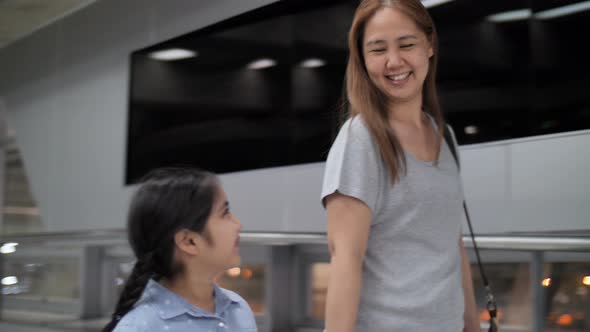 Young Asian girl and mother walking with travel bag at the airport.