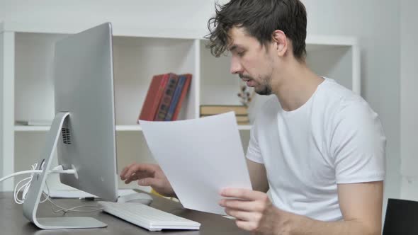 Young Creative Man Reading Documents and Typing On Desktop