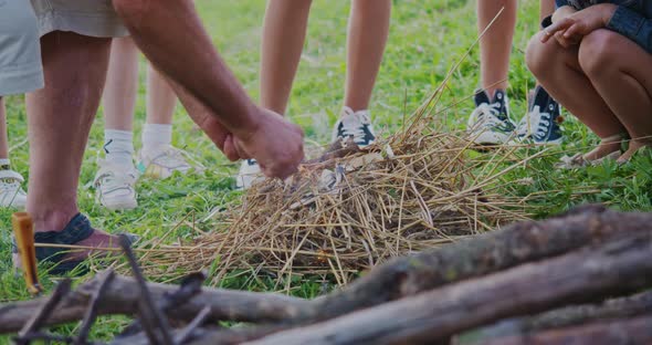 Close Up of Old Man Making Fire From Branches Kids Watching in Campsite