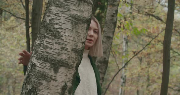 Young Shy Blonde Woman Walks on the Leafs Around a Tree in Autumn. Slow Motion