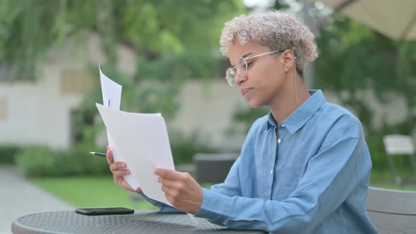 Young African Woman Reading Documents in Outdoor Cafe