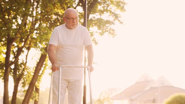 Disabled old man is walking with a walker. Handicapped patient in the park.