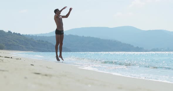 The Handsome Man with a Perfect Athletic Body in Swimming Trunks Having Fun on a Deserted Beach in