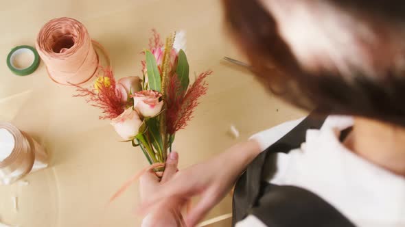 Young Florist Tying Bouquet of Roses and Dried Flowers with Ribbon at Workplace