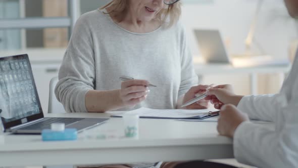 Mid-Aged Woman Signing Medical Document with Female Doctor