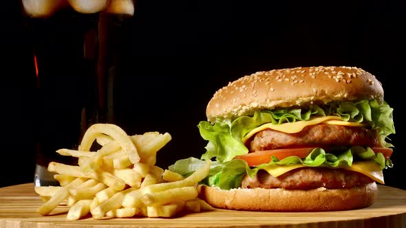 Burger with French Fries and a Glass with Ice Cola on a Black Rustic Background