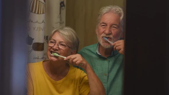 couple of two happy and smiling seniors brushing their teeth of they each other together at home