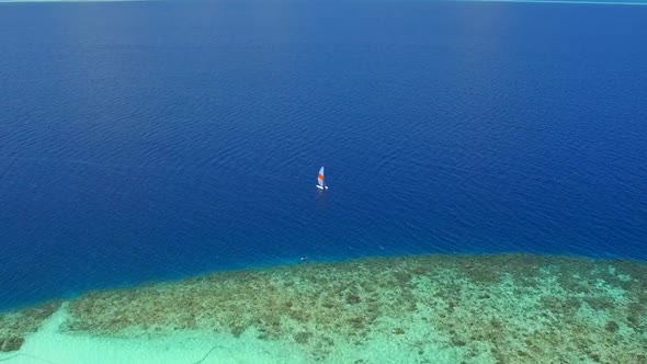 Aerial drone view of a man and woman sailing on a boat to a tropical island.