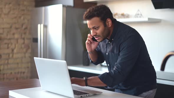 Young Man Checking Something on the Laptop During Phone Conversation