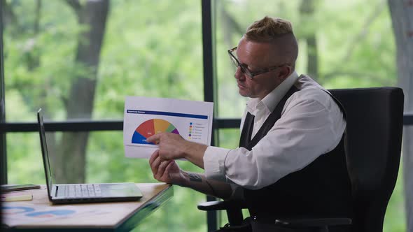 Confident Caucasian Man Showing Diagram Talking at Video Chat on Laptop Sitting in Office Indoors