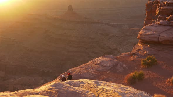 Unrecognizable People Sit on the Edge of Cliff and Enjoy Sunset. Gimbal Shot of Dead Horse Point