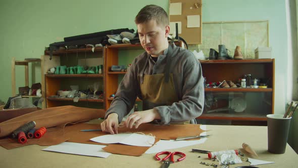 An Experienced Male Tanner Makes a Layout of Bag Elements on a Large Piece of Brown Leather on a