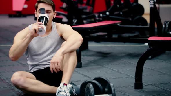 Young Man Athlete Drinking Water From Shaker Bottle in Gym