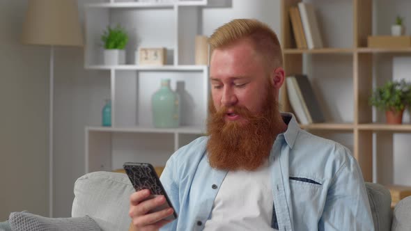 Millennial Attractive Redhead Guy Sit Indoor Use Smartphone Chat in Social Media Share Text Messages