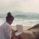 Brunette Woman Sits on Wild Beach Writing in Notebook - VideoHive Item for Sale
