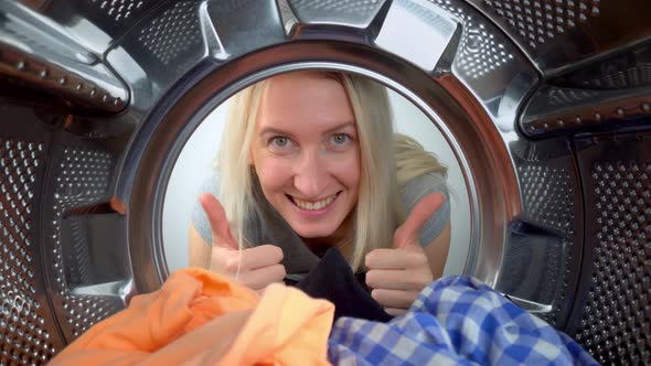 Woman shows sign of approval thumbs up in washing machine. Inside view.