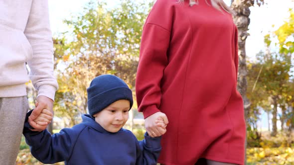 Cute Little Boy Jumps Walking with Parents Along Autumn Park