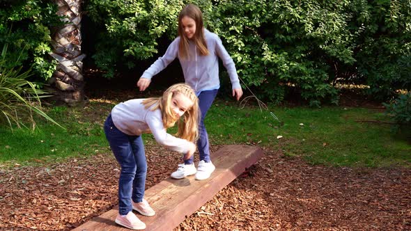 Two Girls Teetering on an Unstable Log Playing in the Park