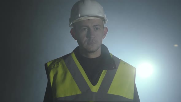 Portrait of the Engineer in the Builders Uniform and Helmet on a Black Background in the Spotlight