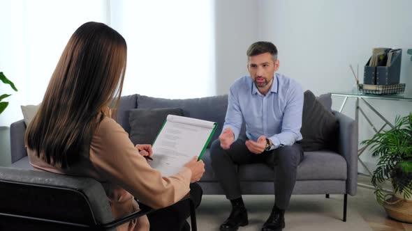 Psychologist Listens Client Taking Notes on Clipboard at Psychotherapy Session