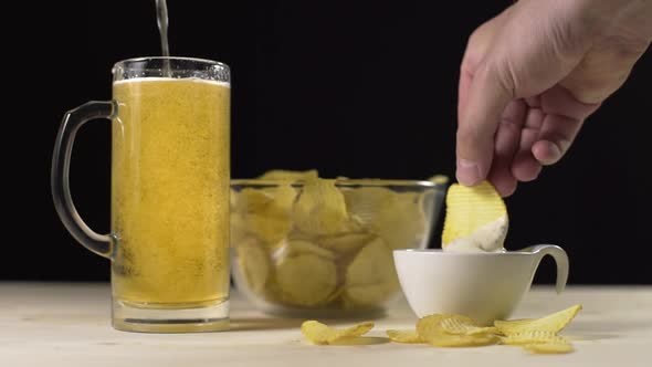 Golden Beer Is Poured in Slowmotion To the Glass, Man Takes Potato Chips and Dips Them in the Sauce