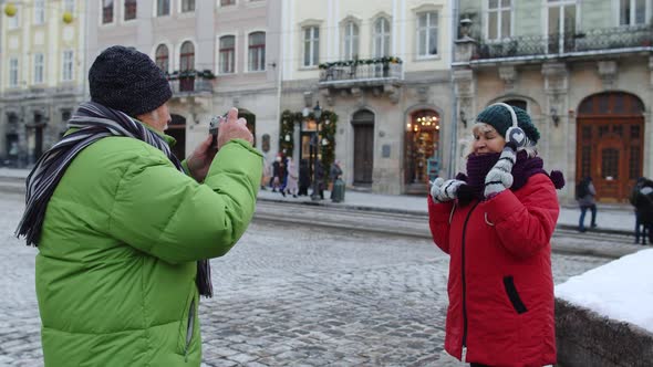 Senior Couple Man Woman Tourists Grandfather Taking Photo Pictures of Grandmother on Retro Camera