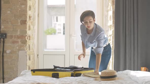 Portrait of Positive Beautiful Caucasian Woman Packing Yellow Suitcase Before Trip. Young Gorgeous