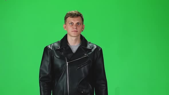 Young Man in Black Leather Jacket Going and Looking Forward Against a Green Background, Slow Motion