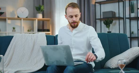 Modern Man Sitting on Comfortable Sofa at Home and Working