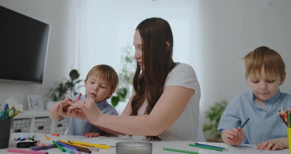 A Young Mother with Two Children Sitting at a White Table Draws Colored Pencils on Paper