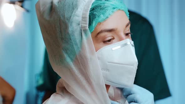 Female Doctor Putting on a Medical Cap, Protective Mask KN95, Glasses and Hazmat
