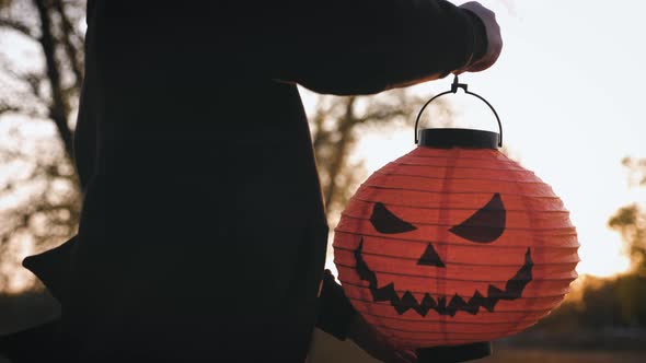 Little Boy Having Fun with Halloween Carved Pumpkin in a Park at Dusk