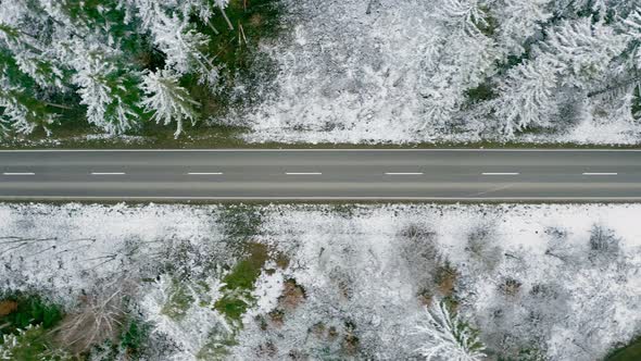 Drone flight over a empty street in a snow covered forest captured straight from above at times of t