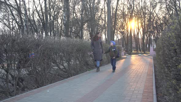 Wide Shot of Young Caucasian Woman and Schoolboy Walking Along the Alley in Park on Sunset and