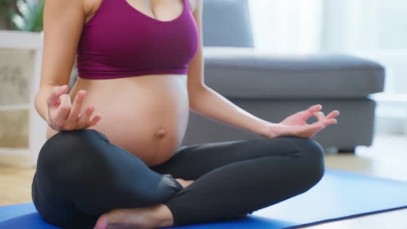 Asian young pregnant woman doing yoga pilates workout in living room.