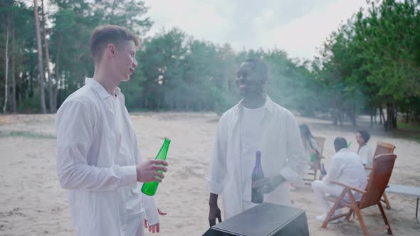 Young Men Talk While Cooking Barbecue at the Party Drinking From Bottles