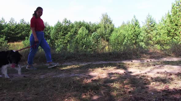 Young Woman Walking with Her Dog on a Leash on Nature