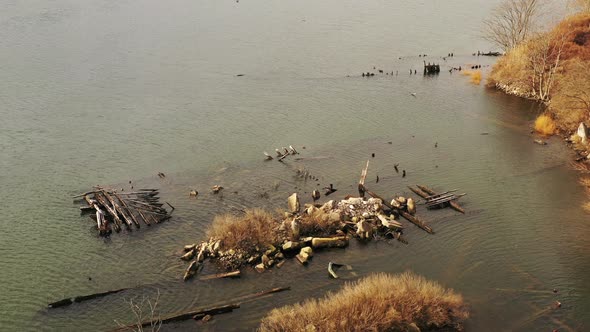 an aerial dolly shot backwards over an old sunken wooden pier in a creek. The camera then tilts up t