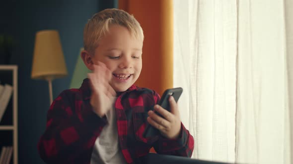 Cute Little Boy with Blond Hair is Speaking Via Video with His Grandma and Waving Hello to the