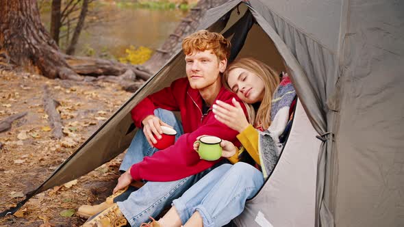 Young Man and Woman in Casual Outfit are Smiling Holding Cups of Tea Cuddling Sitting in Tent Near