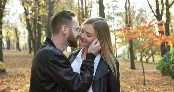 Happy Man Kisses His Cheerful Girlfriend in Sunny Autumn Park